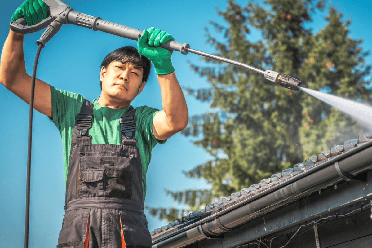 Technician power cleaning the gutters of a roof