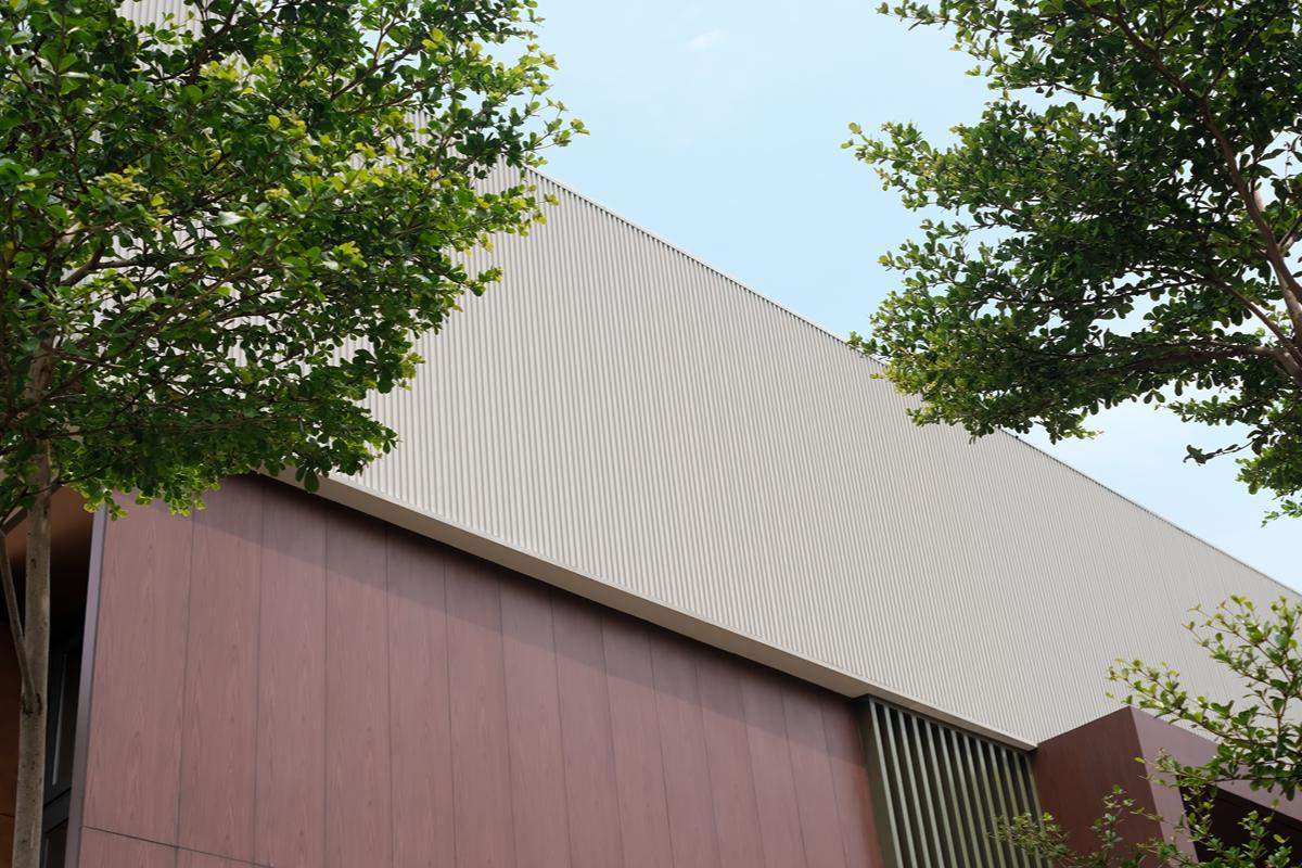 Light-colored ribbed metal wall cladding installed on a contemporary building surrounded by trees