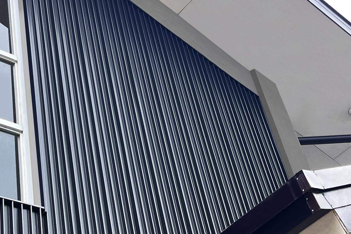 MTL-0726A-FEAT Dark vertical metal wall cladding installed on a modern building exterior beneath a covered roof